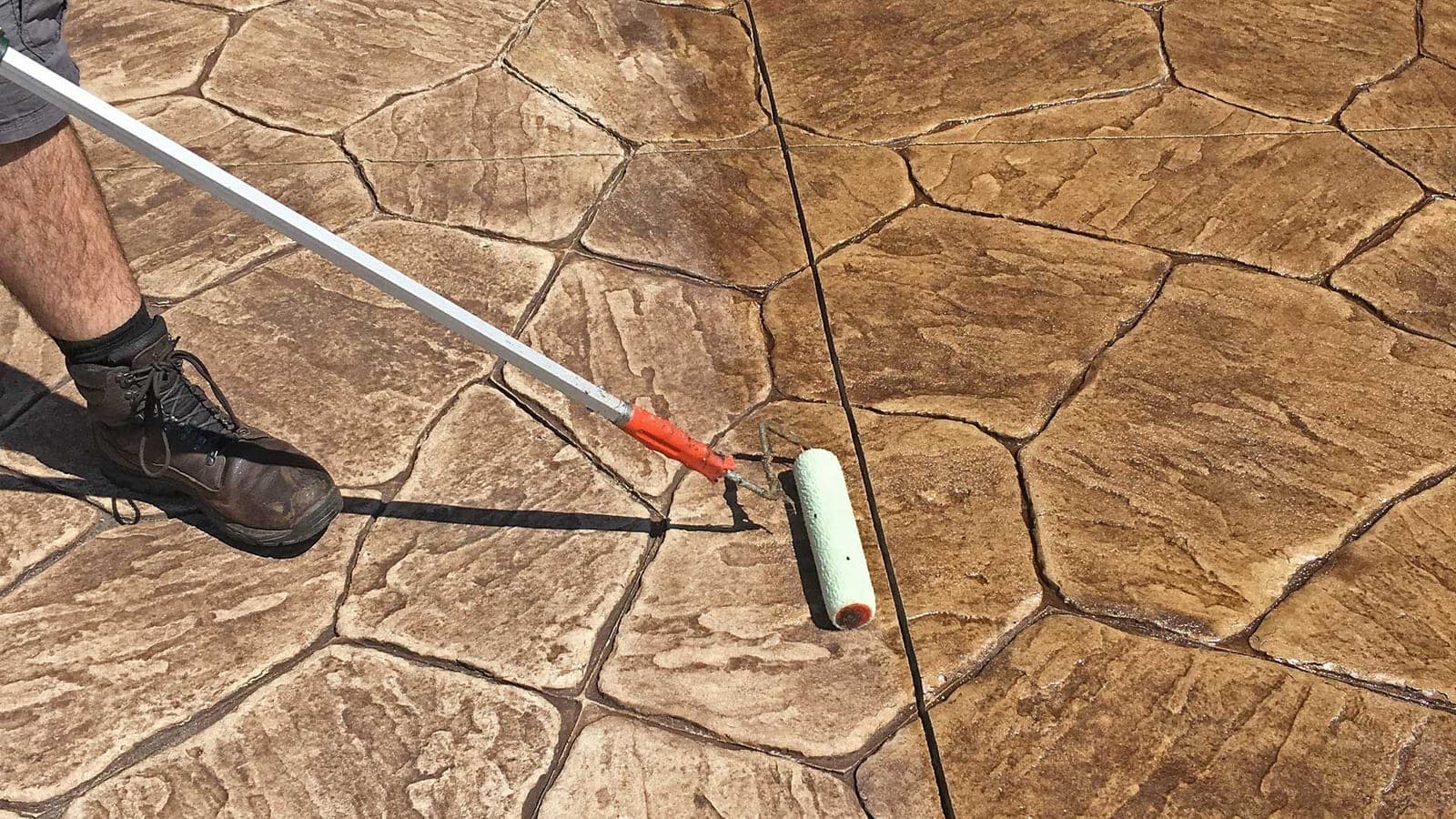 Roller applying solvent-based sealer to stamped flagstone concrete